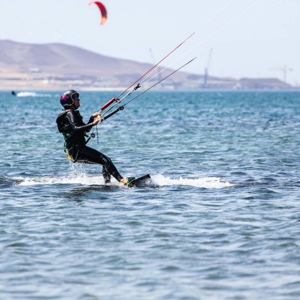 Beginner female kitesurfer making her first steps on the board and riding to the right on a flat water bay during the Kite Sisters Women Kiteboarding Camp in Paracas Peru
