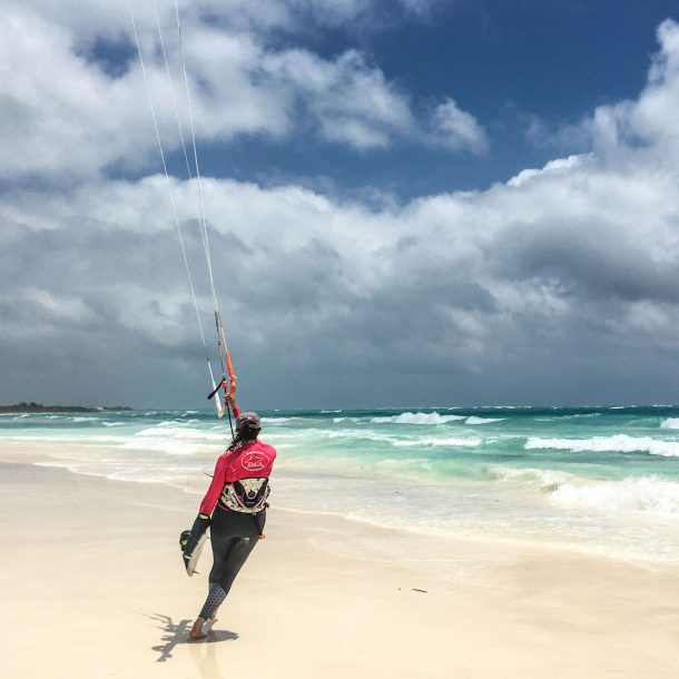 Kitesurfer flying a kite and holding a board on the other hand, while she runs to the water to start kiteboarding during the Kite Sisters Women Kiteboarding Camp in Tulum
